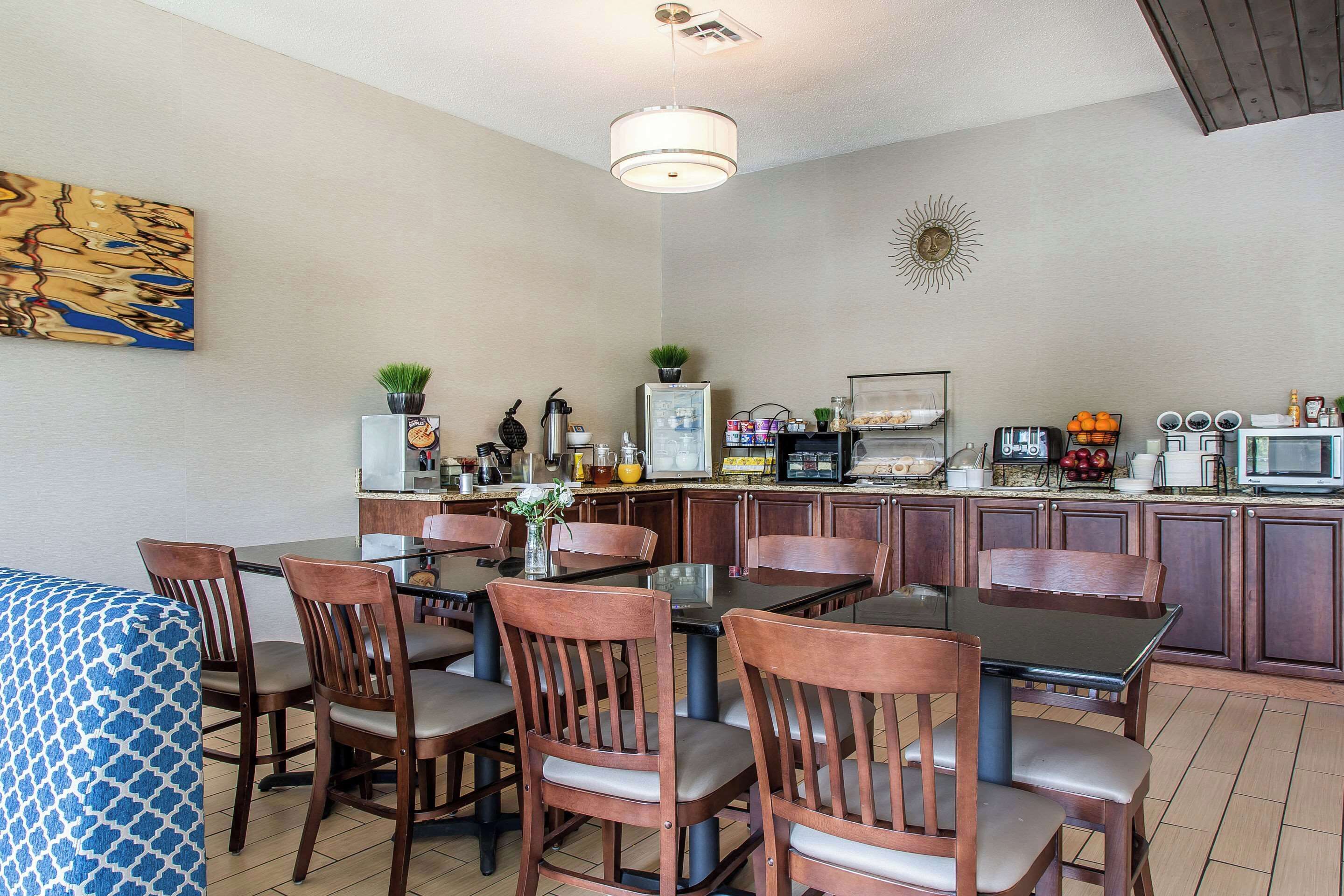A dining area with wooden chairs and a glass table, a kitchen with cabinets and appliances, and a painting on the wall.