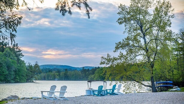 A lakeside setting with Adirondack chairs and a covered seating area, surrounded by trees and hills in the background. - The Black Swan Lee - Lenox, an Ascend Collection Hotel (Lee)