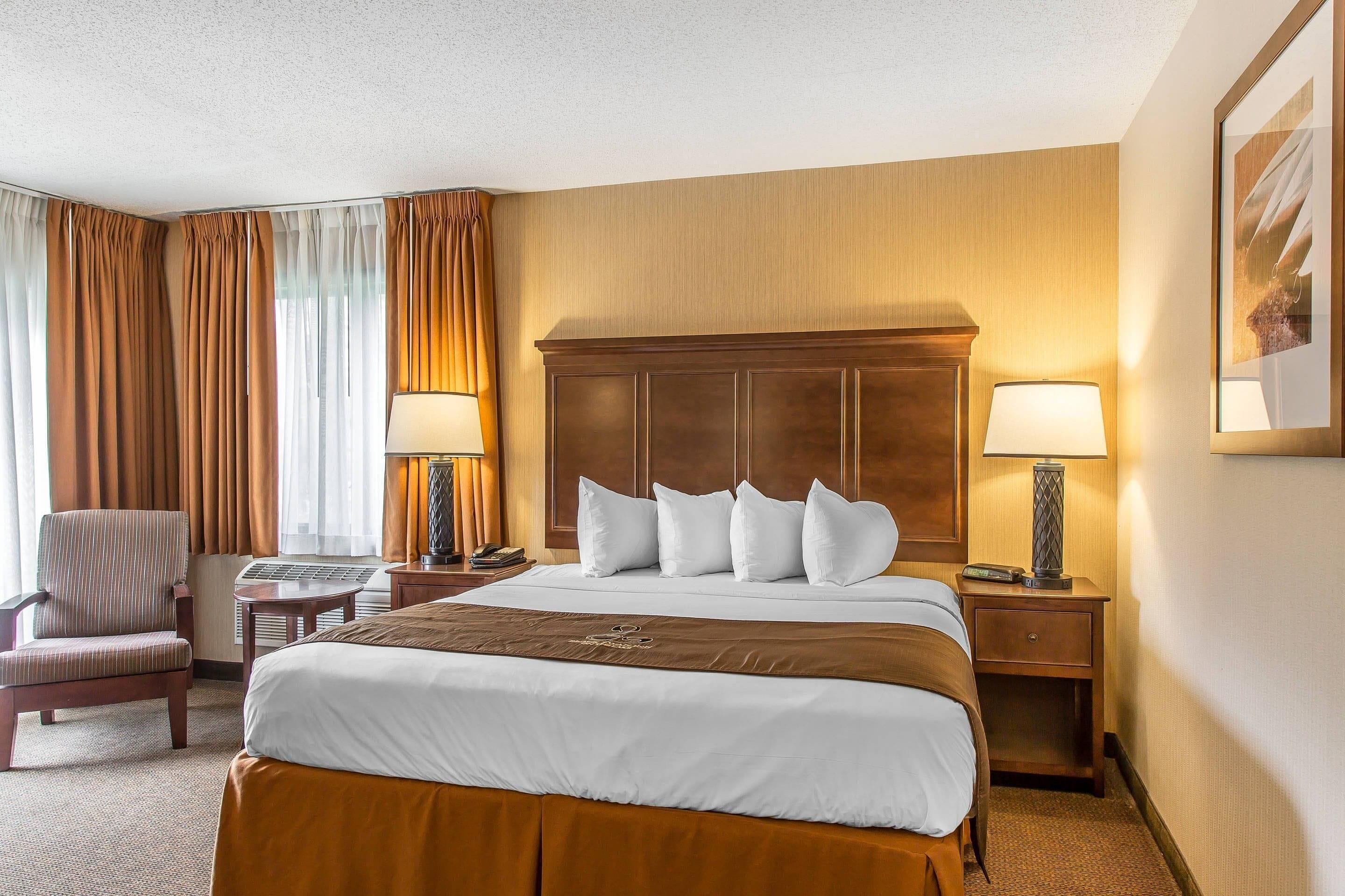 Une chambre d’hôtel avec un grand lit, deux tables de chevet avec des lampes, une chaise et un bureau avec un clavier.