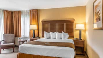 A hotel room with a large bed, two bedside tables with lamps, a chair, and a desk with a keyboard.