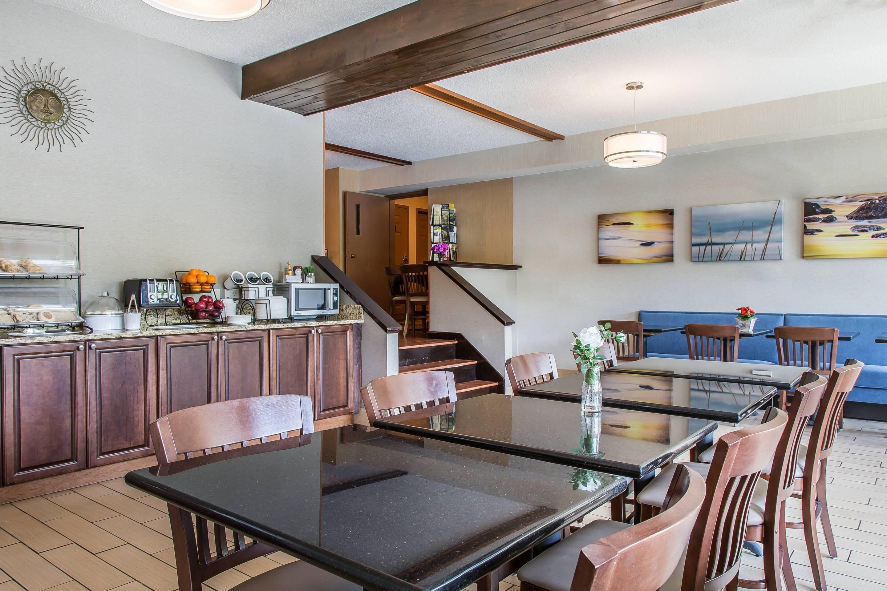 Una cocina moderna con armarios de madera, un comedor con mesa de vidrio y una escalera que lleva a una sala de estar con sofá azul y obras de arte en la pared.