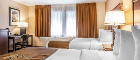 A hotel room with two beds, a desk, a chair, and a lamp.
