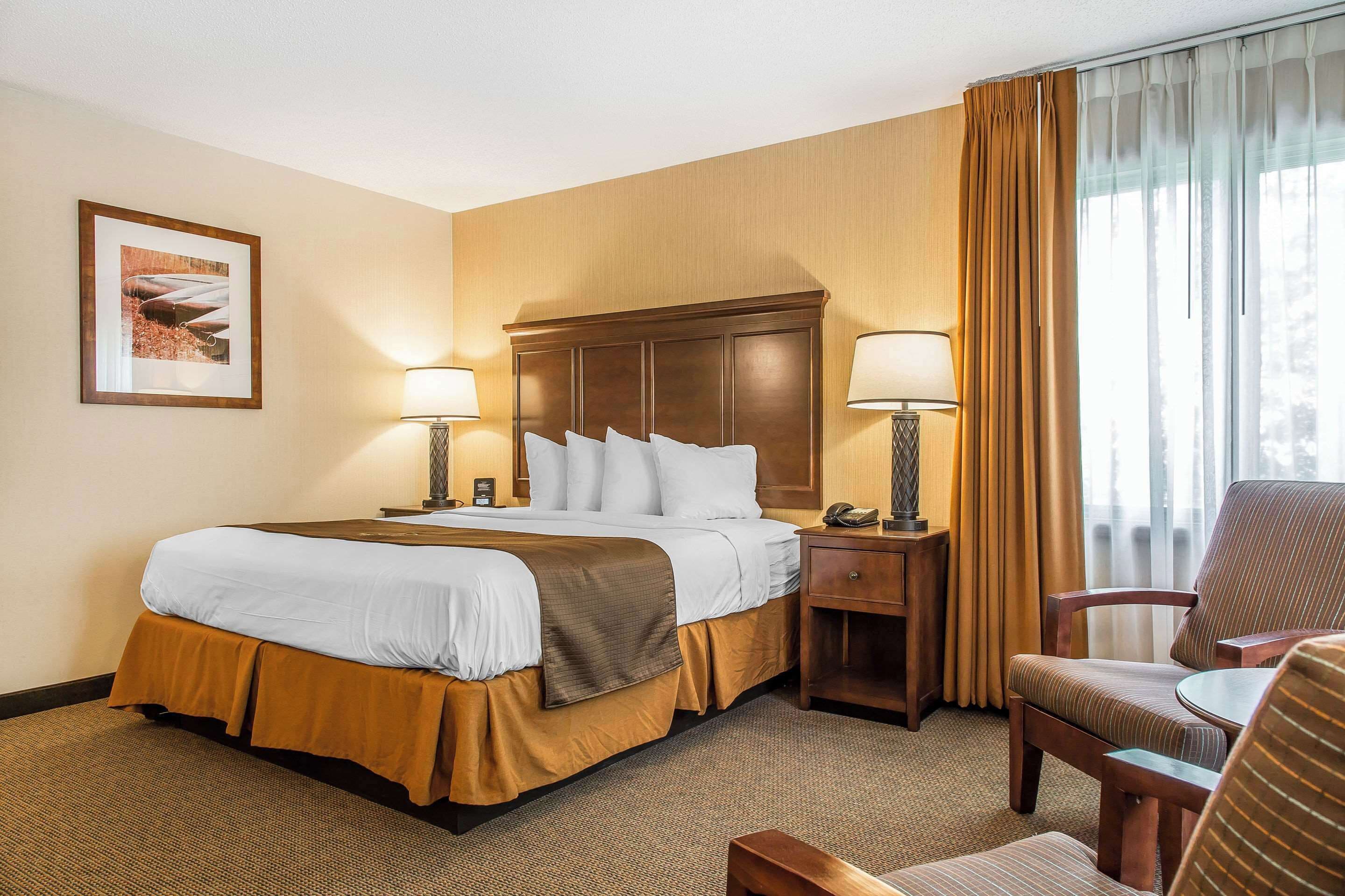 A hotel room with a large bed, two bedside tables with lamps, a chair, and a framed picture on the wall.