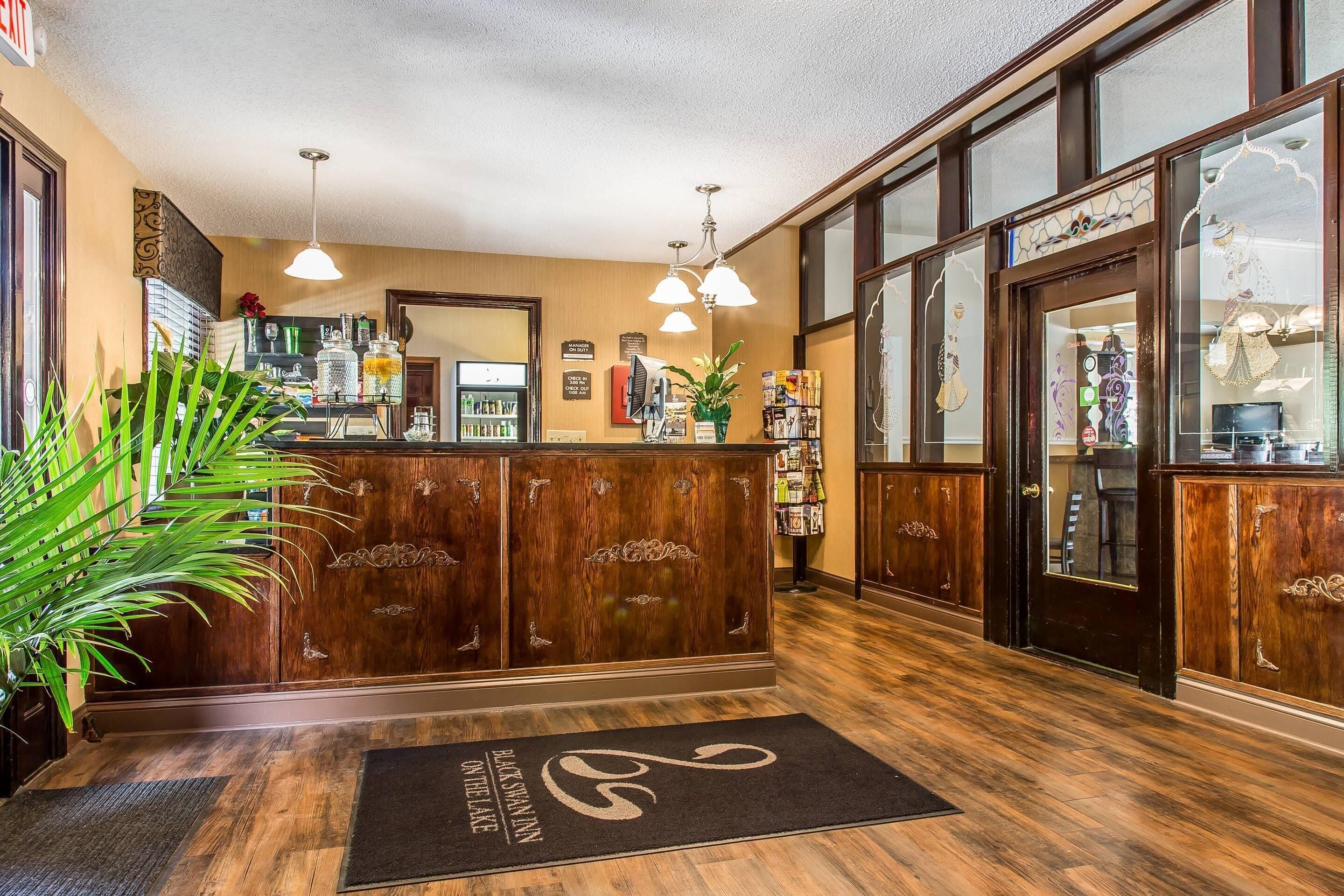 A reception area with a wooden reception desk, a black doormat, and a large potted plant.