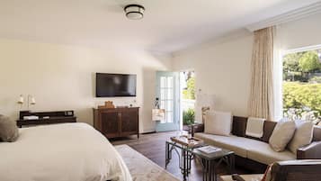 Une chambre d’hôtel avec un lit, un canapé, une télévision et une vue sur la verdure environnante.