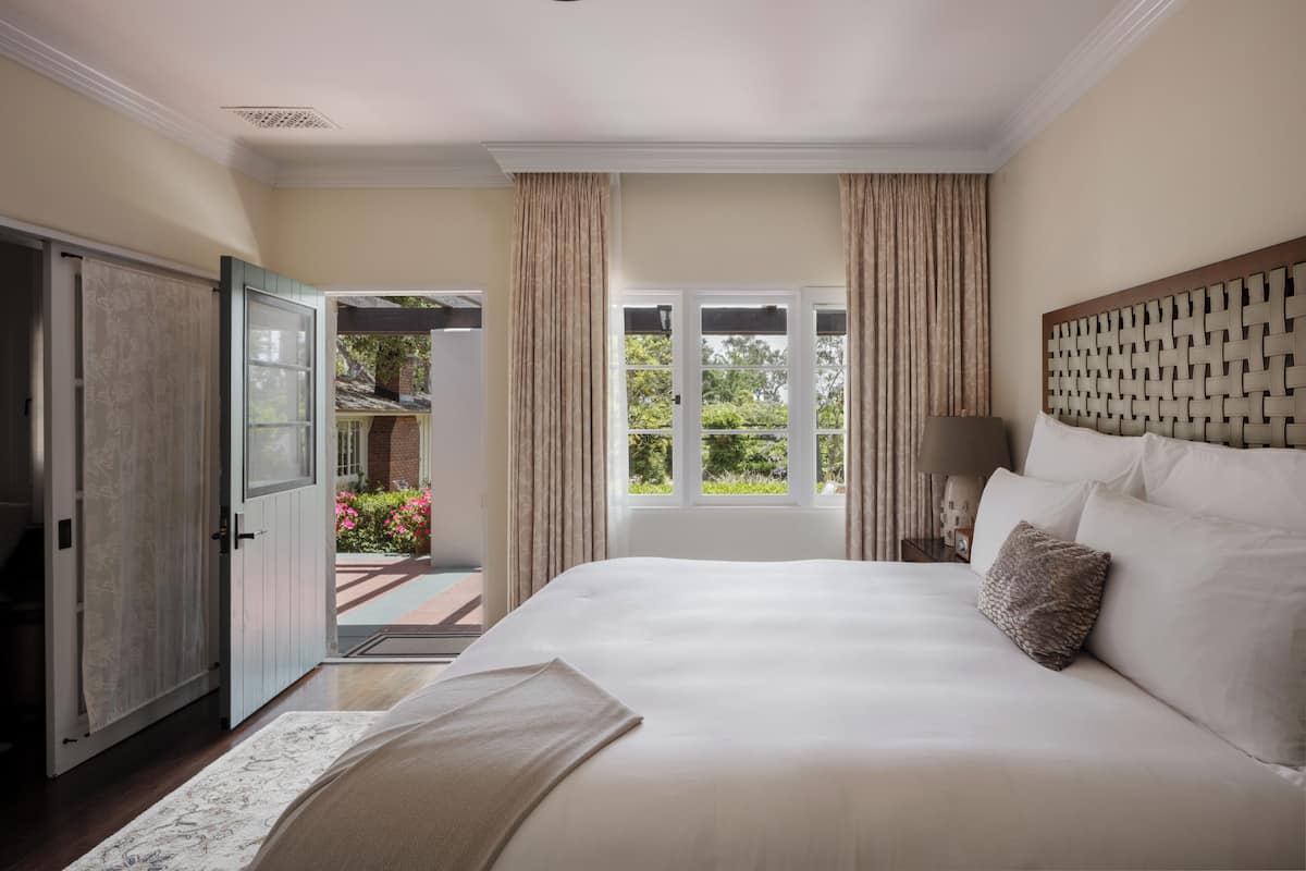 A bedroom with a large bed, a view of the garden, and a door leading outside.