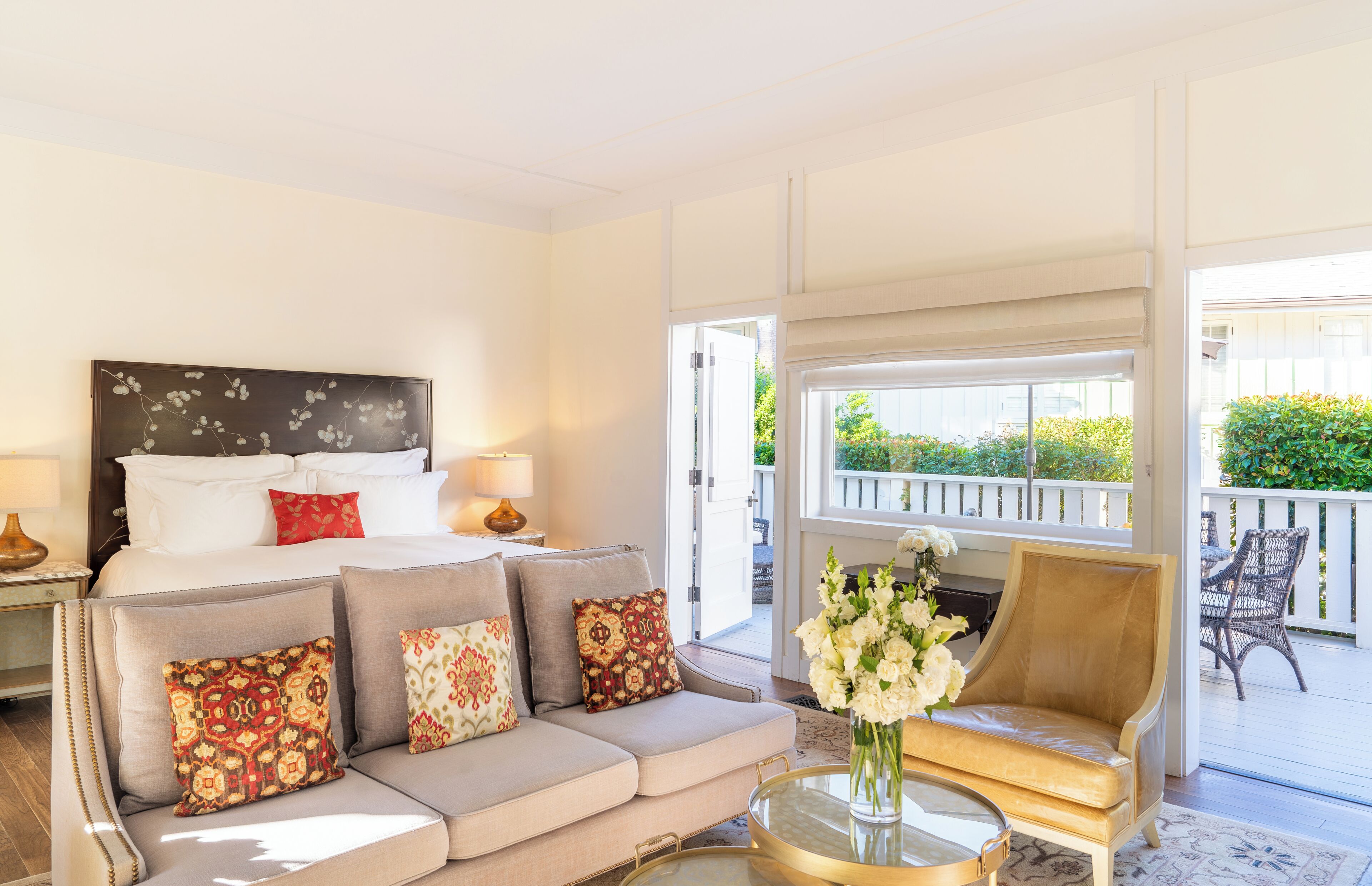 Une chambre d’hôtel comprenant un lit, un canapé, une chaise, une table avec un vase de fleurs et un balcon aménagé avec du mobilier d’extérieur.