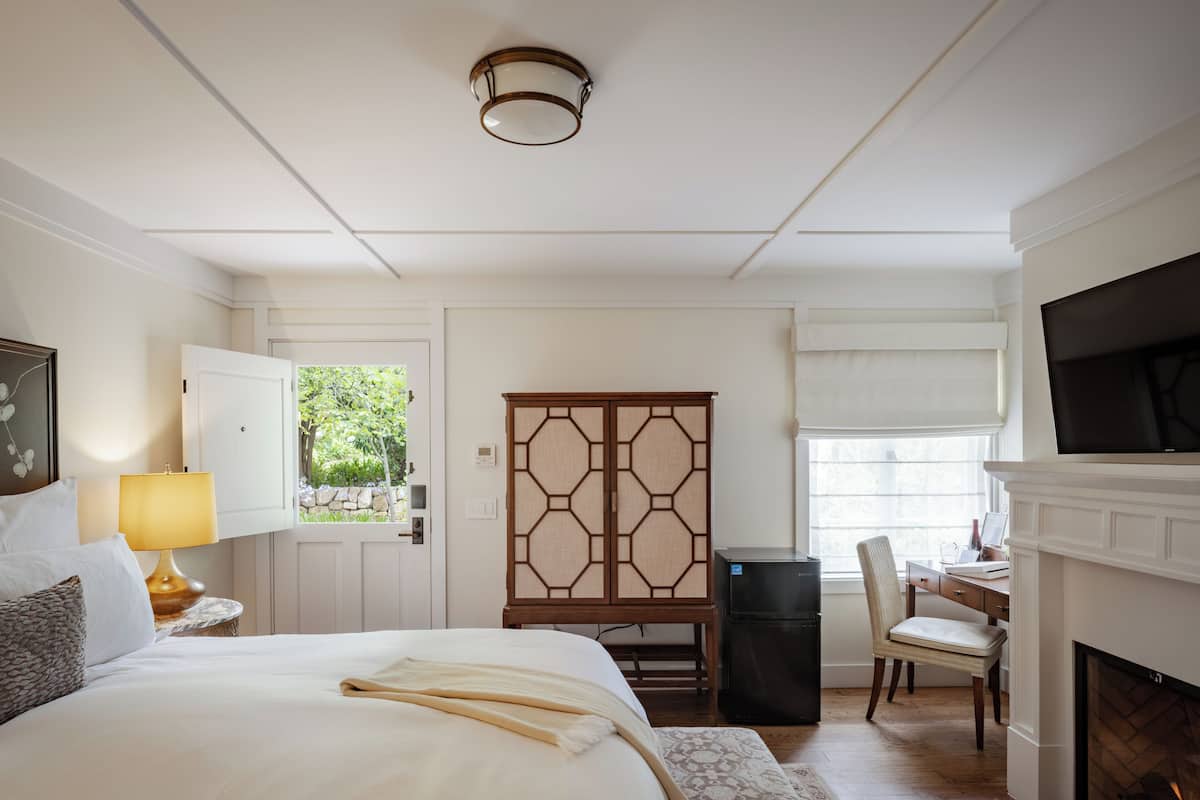 A hotel room with a bed, a desk, a chair, a fireplace, and a TV.