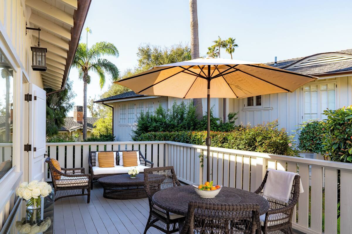 A covered outdoor patio with wicker furniture, a table with a bowl of fruit, and a large umbrella.