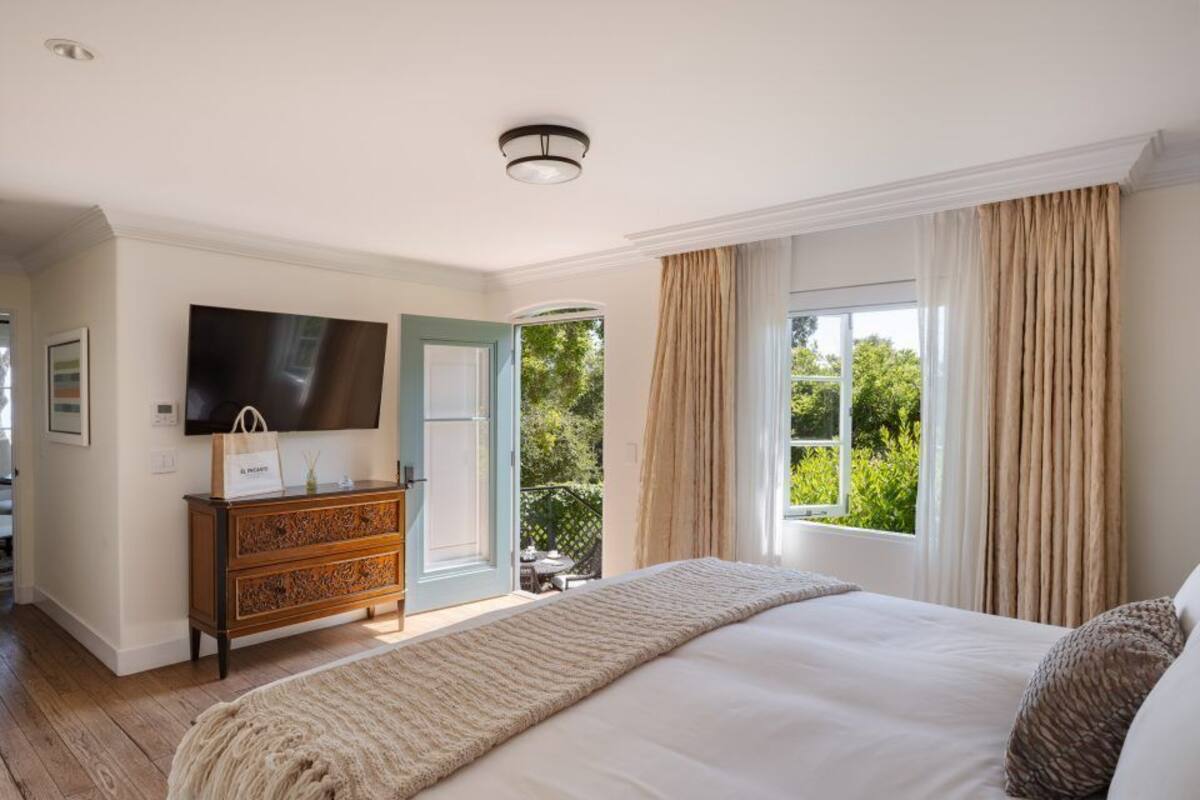 A bedroom with a large bed, a dresser, a flat-screen TV, and a door leading to a balcony.
