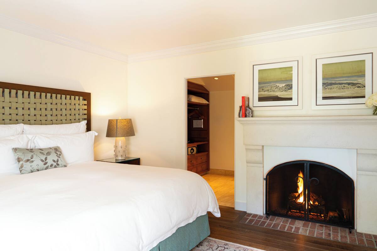 A bedroom with a large bed, a bedside table with a lamp, a fireplace, and a closet.