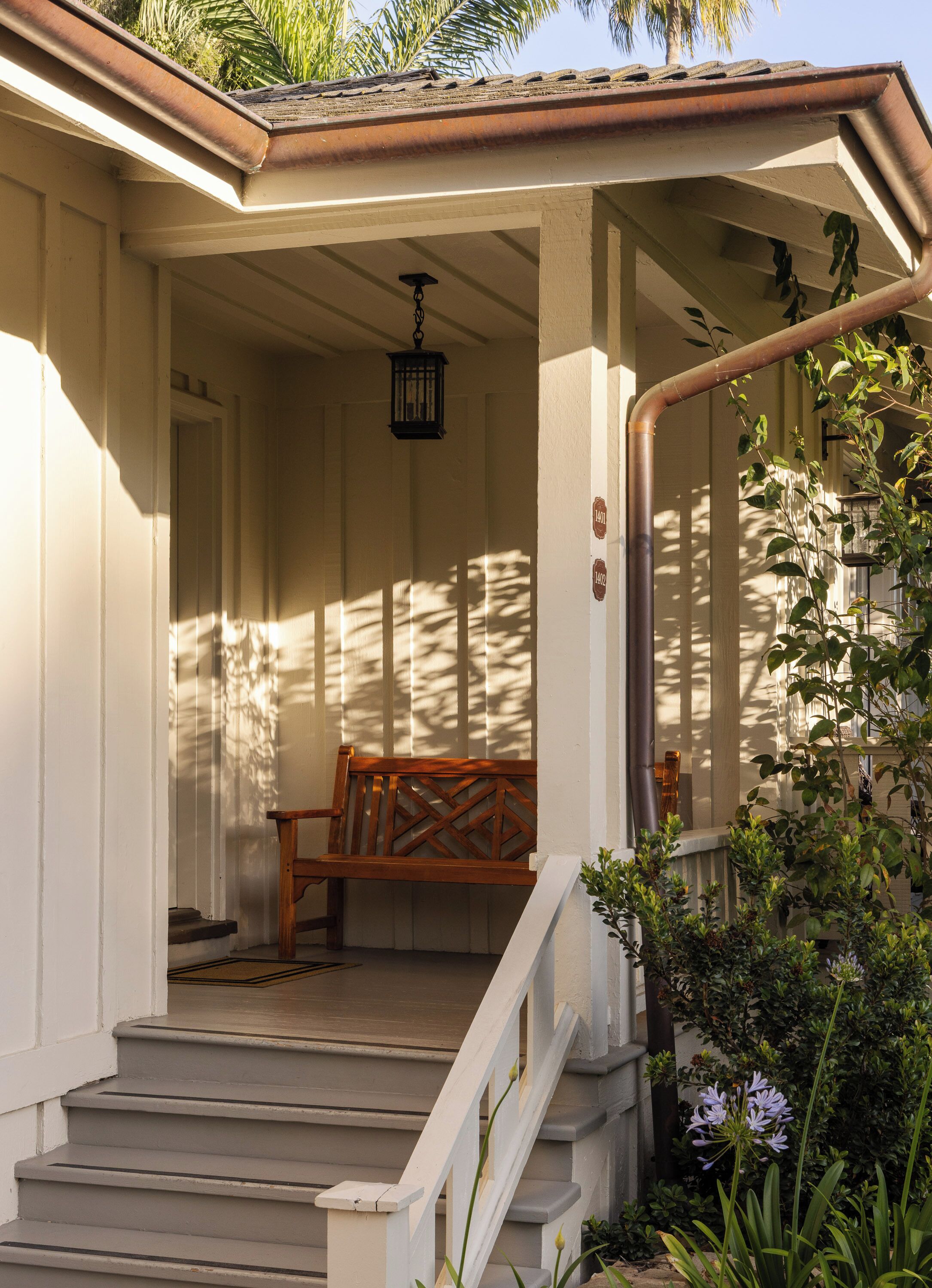A covered porch with a wooden bench, a staircase, and a hanging lantern.