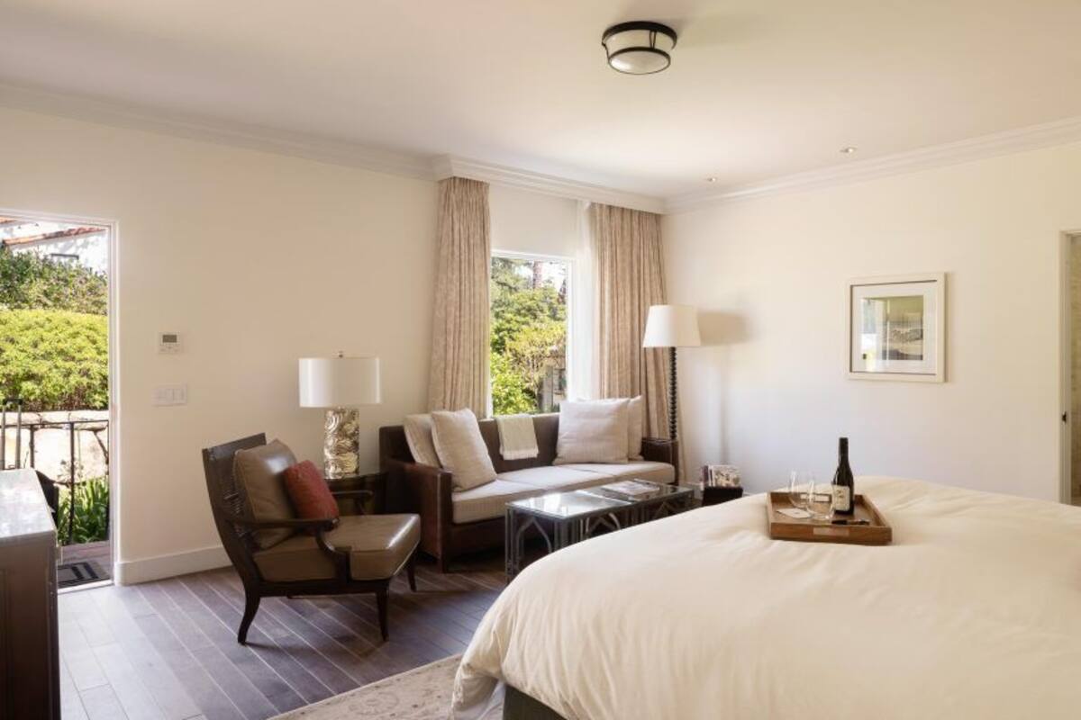 A hotel room with a bed, a sofa, a chair, a table, and a lamp.
