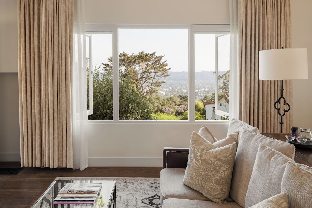 A living room with a sofa, a coffee table with magazines, a lamp, and a view through a window.