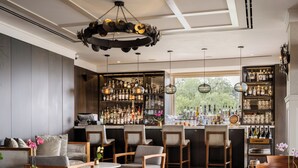 A bar area with wooden chairs, a round table, and a variety of bottles and glasses on shelves. - El Encanto Santa Barbara (Santa Barbara)