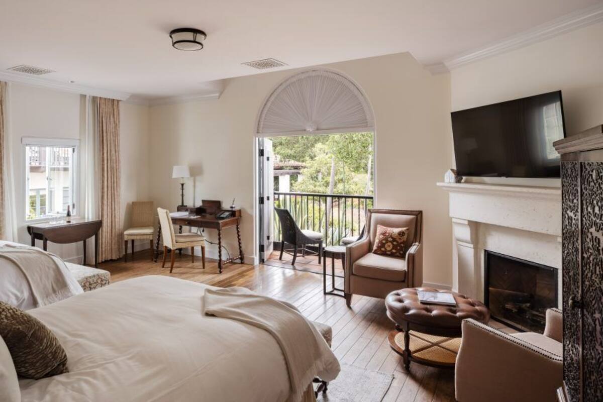 A hotel room with two beds, a desk, a chair, a fireplace, and a TV.