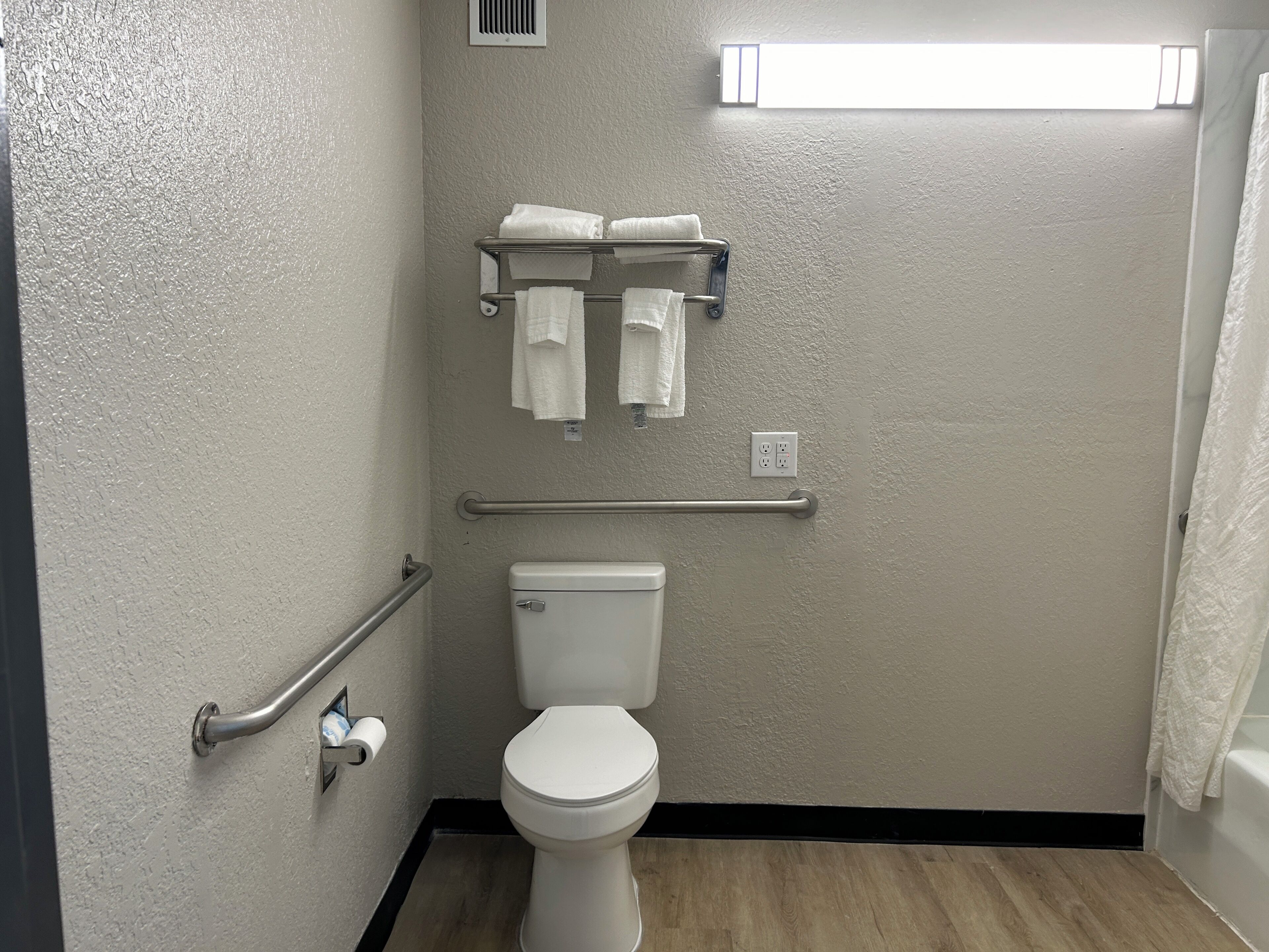 A bathroom with a toilet, a towel rack, a handrail, and a light fixture.