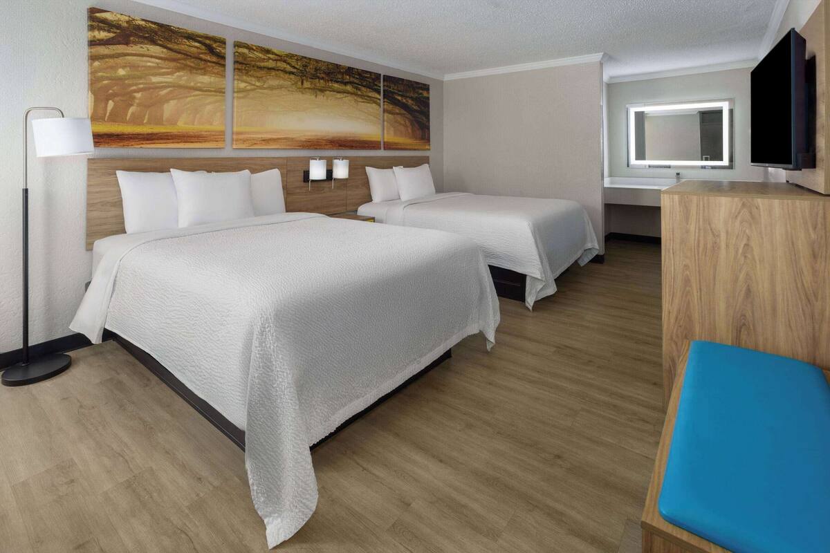 A hotel room with two beds, a desk, a TV, and artwork on the wall.