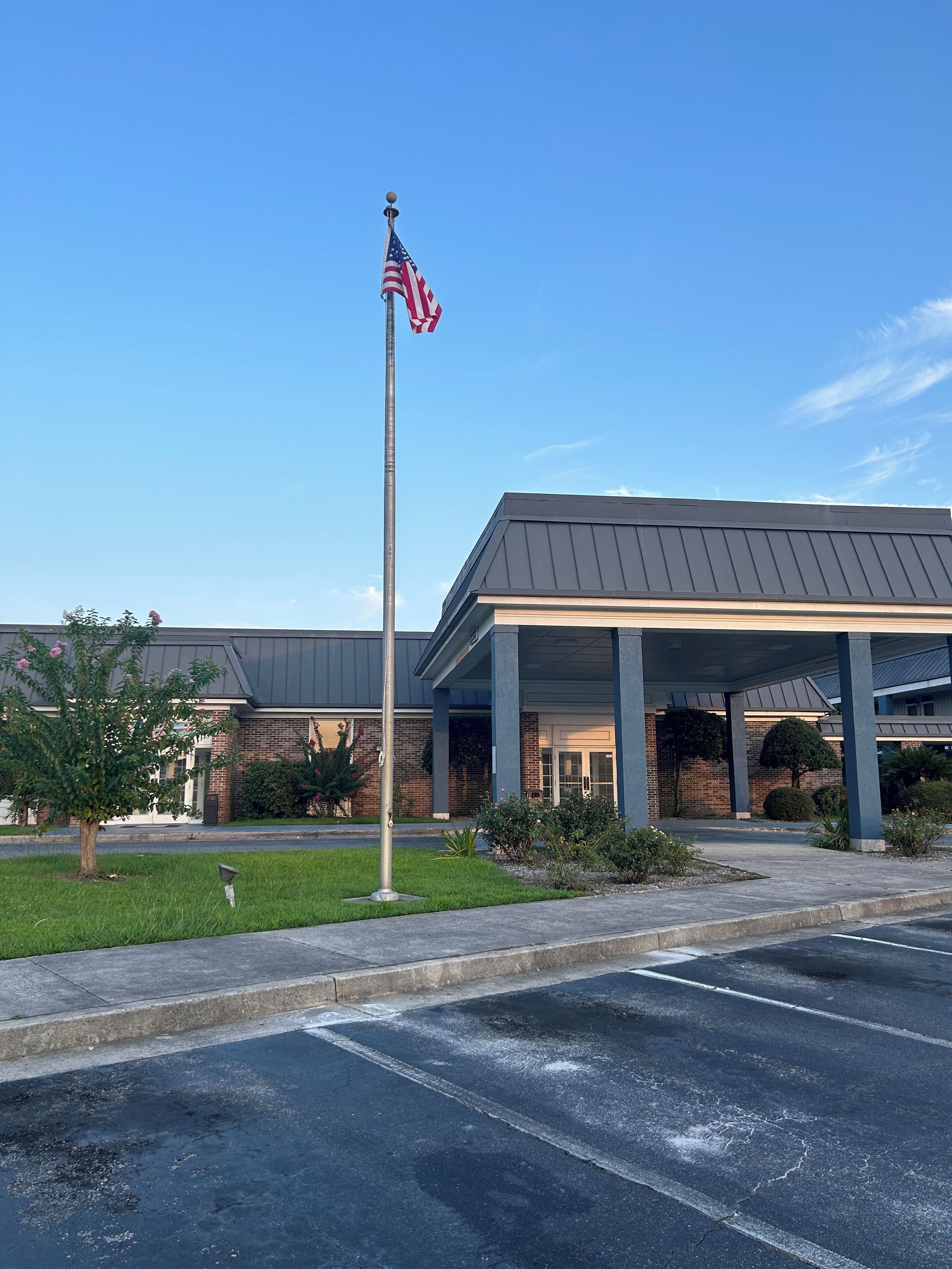 A building with a covered entrance, a flagpole with an American flag, and a parking lot.
