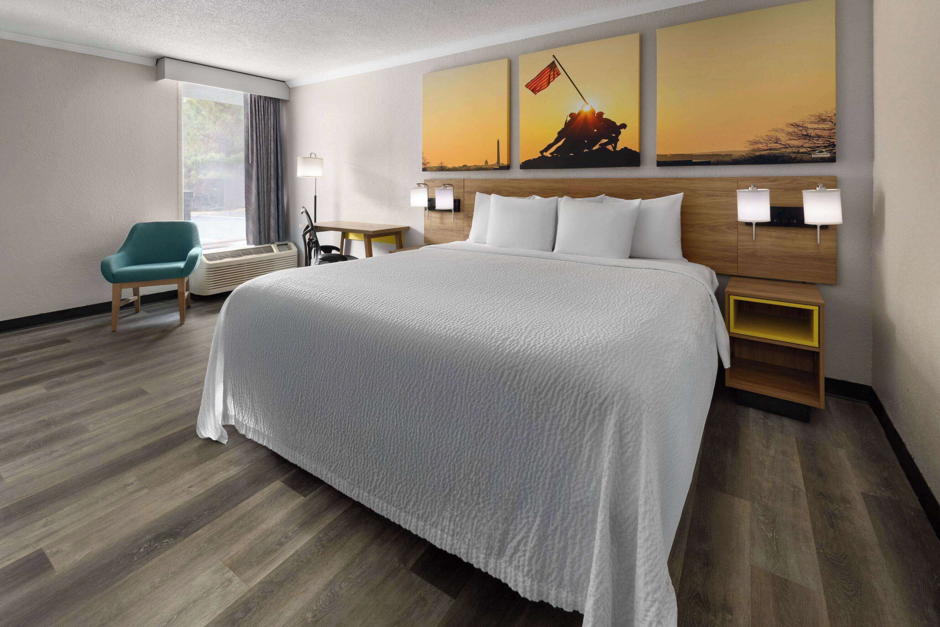 A hotel room with a large bed, a desk, a chair, and a window with curtains.