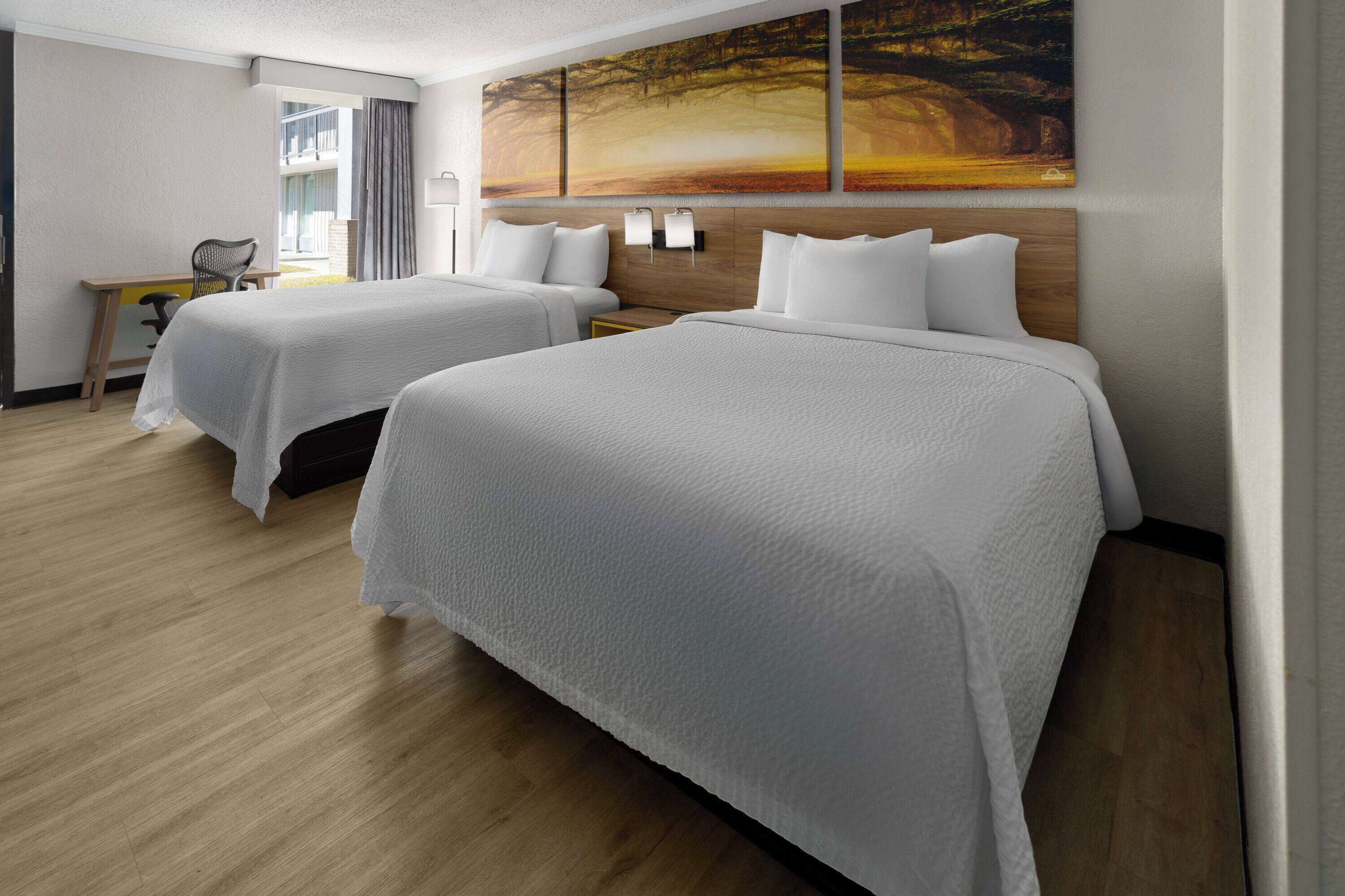 A hotel room with two beds, a desk, and a large painting on the wall.