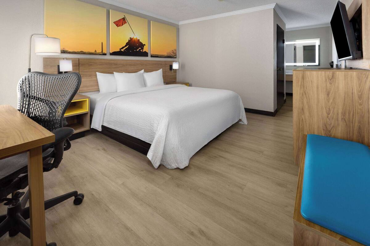 A hotel room with a large bed, a desk with a chair, a TV, and artwork on the wall.