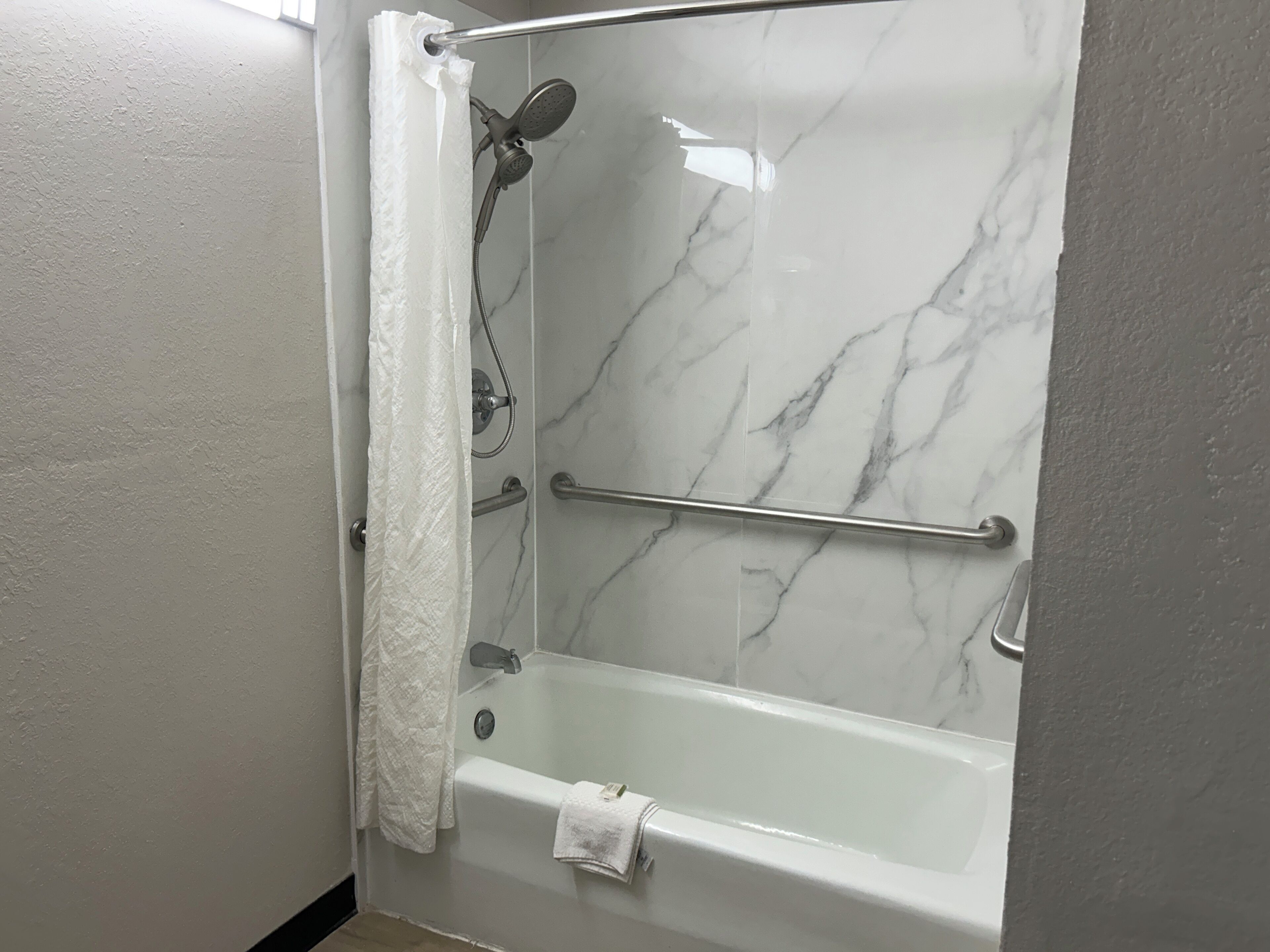 Une salle de bain moderne dotée d’une douche à parois de verre, de murs en marbre et d’une barre d’appui.
