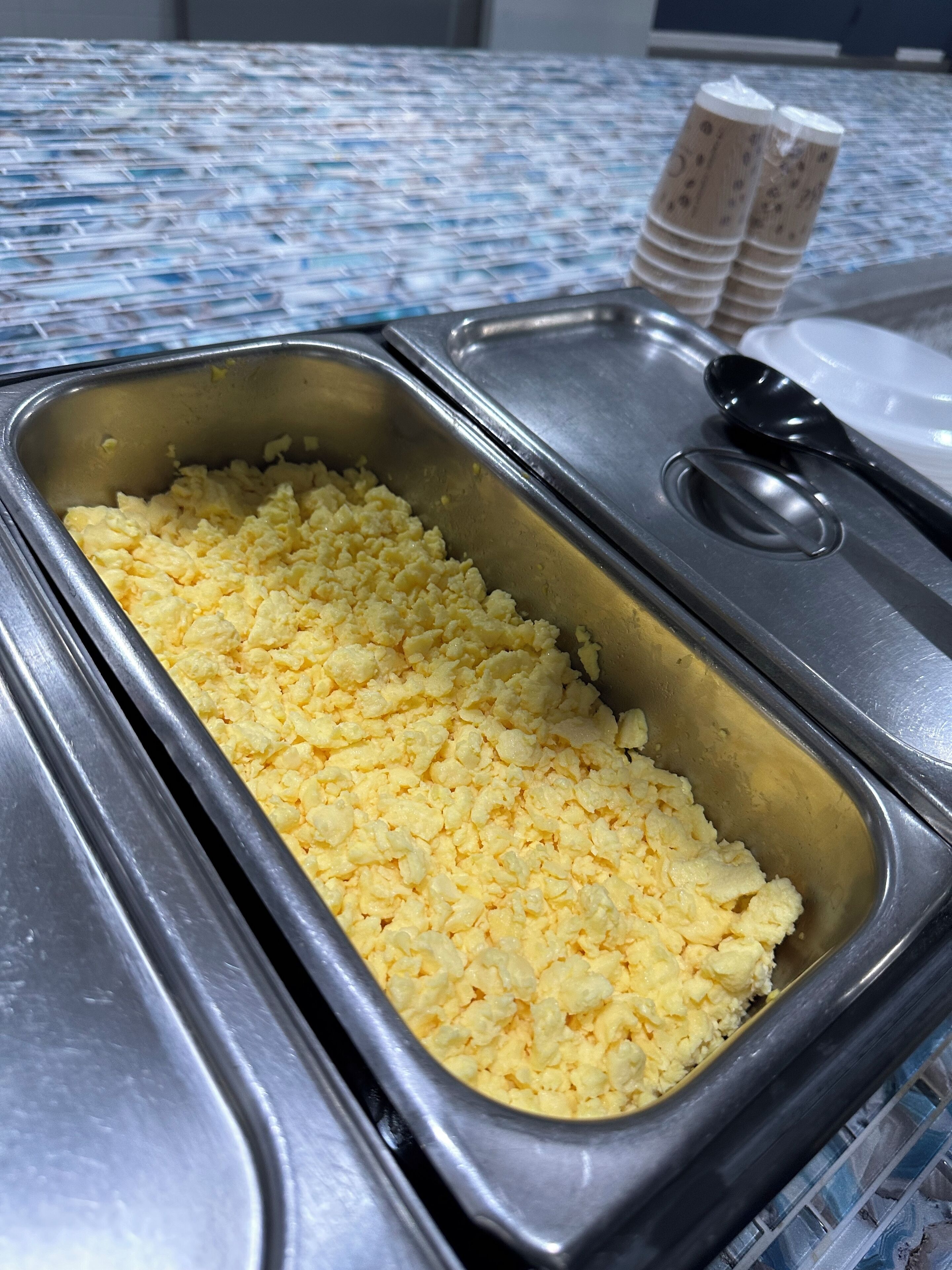 A buffet area with scrambled eggs in a metal serving tray.