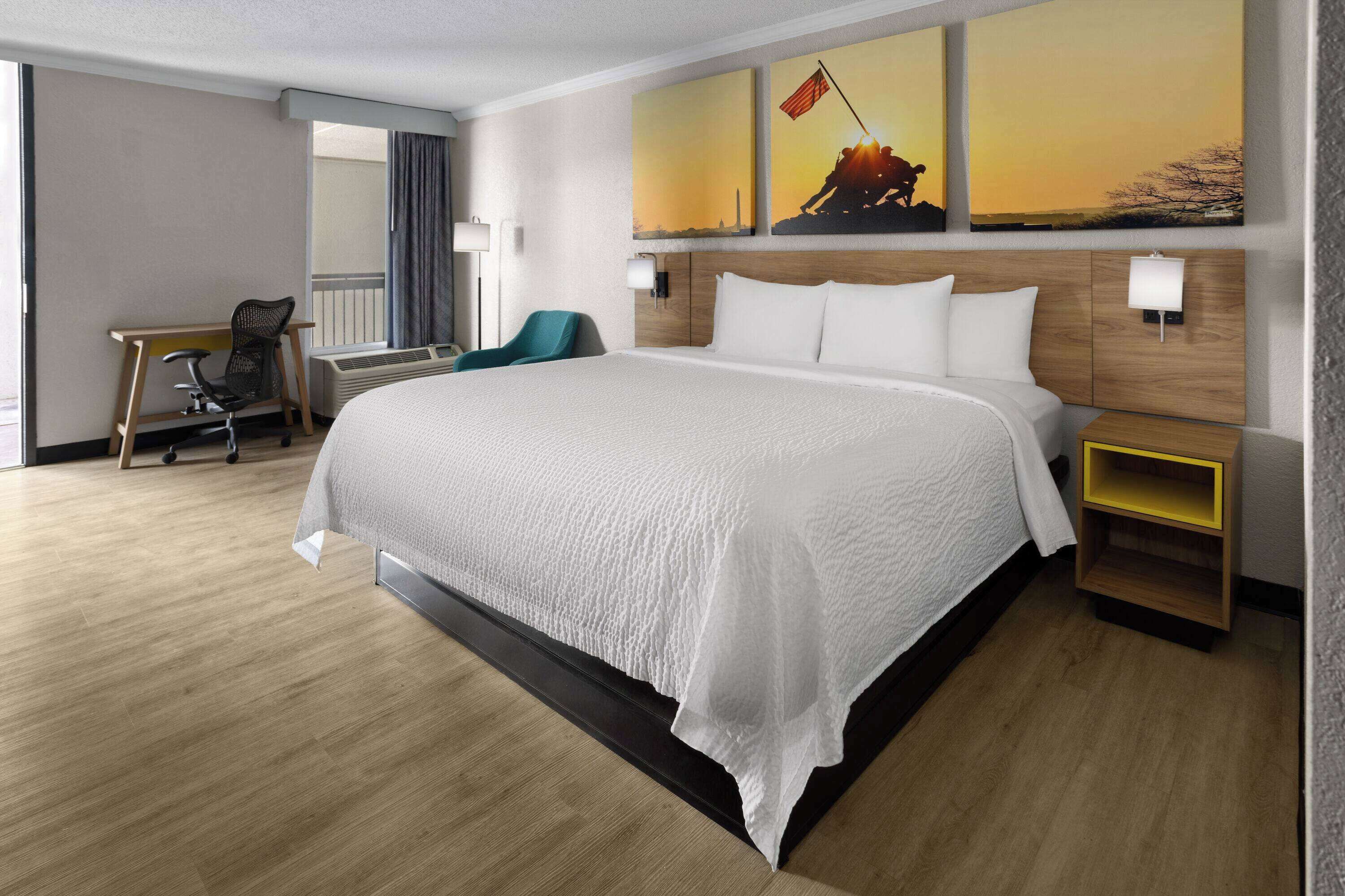 Habitación de hotel con una cama grande, un escritorio con silla, una mesita pequeña y una mesita de noche.