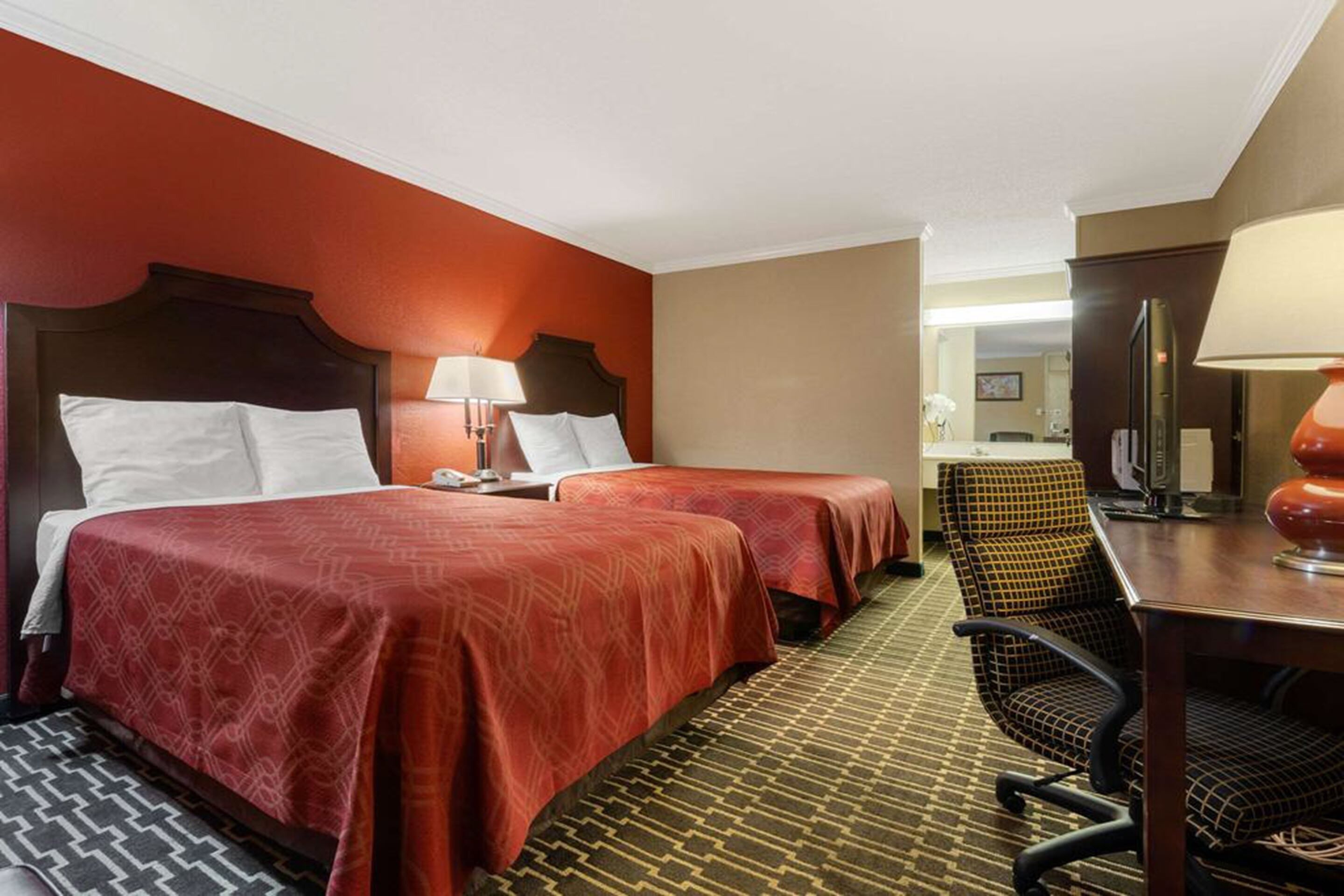 Une chambre d’hôtel avec deux lits, un bureau avec une chaise et un miroir.