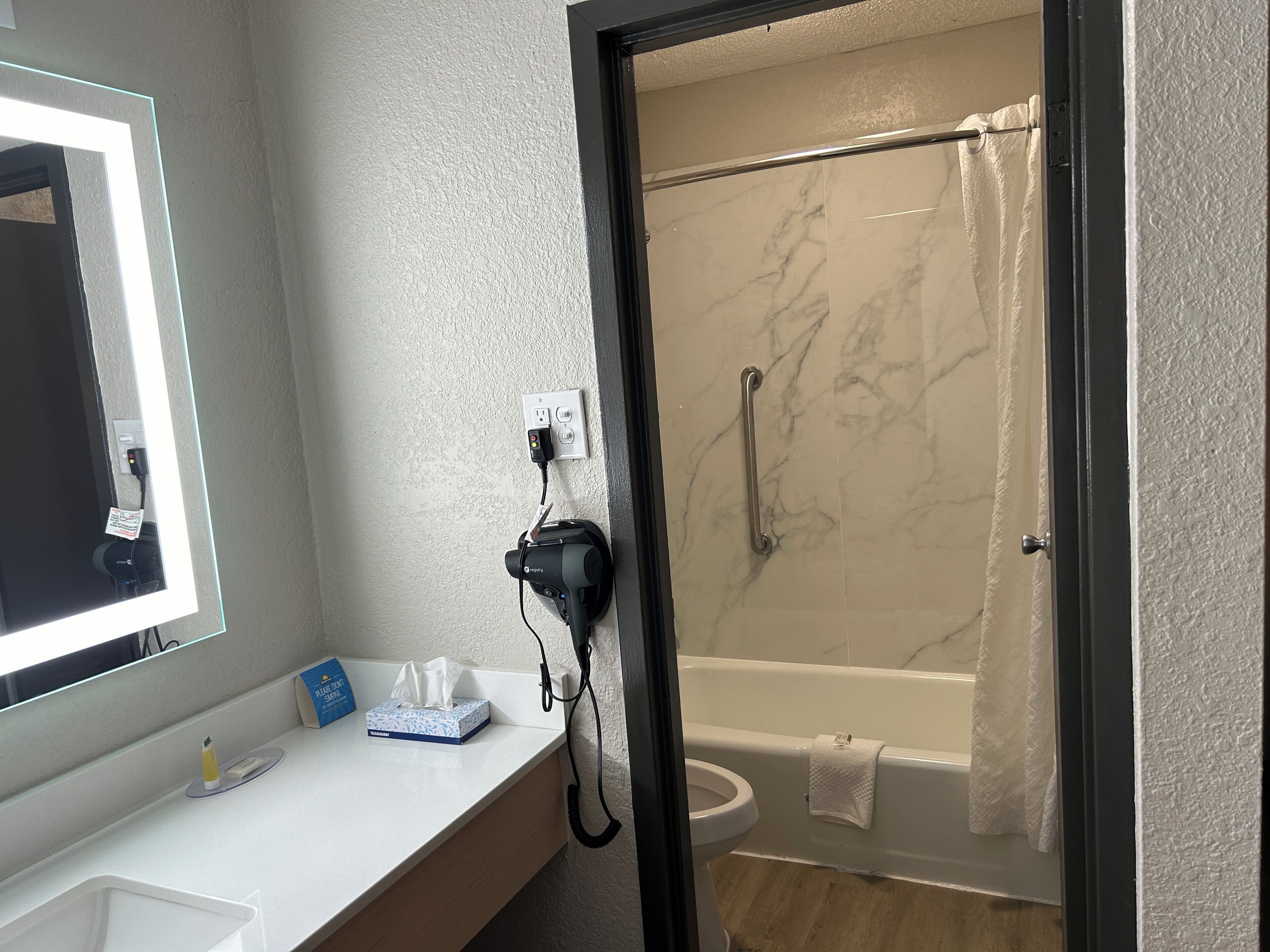 A bathroom with a white sink, a mirror, a hairdryer, a towel rack, and a shower with a glass door.