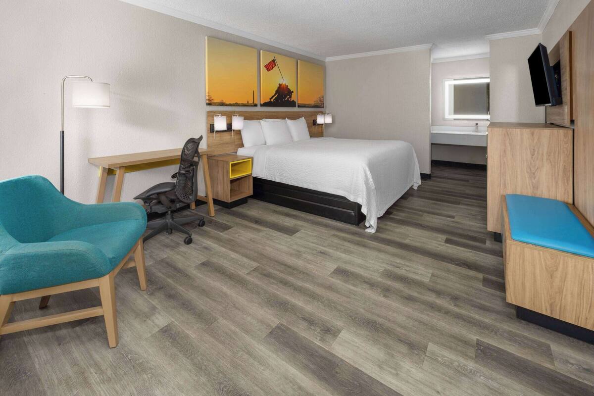 A hotel room with a bed, desk, chair, and a TV.