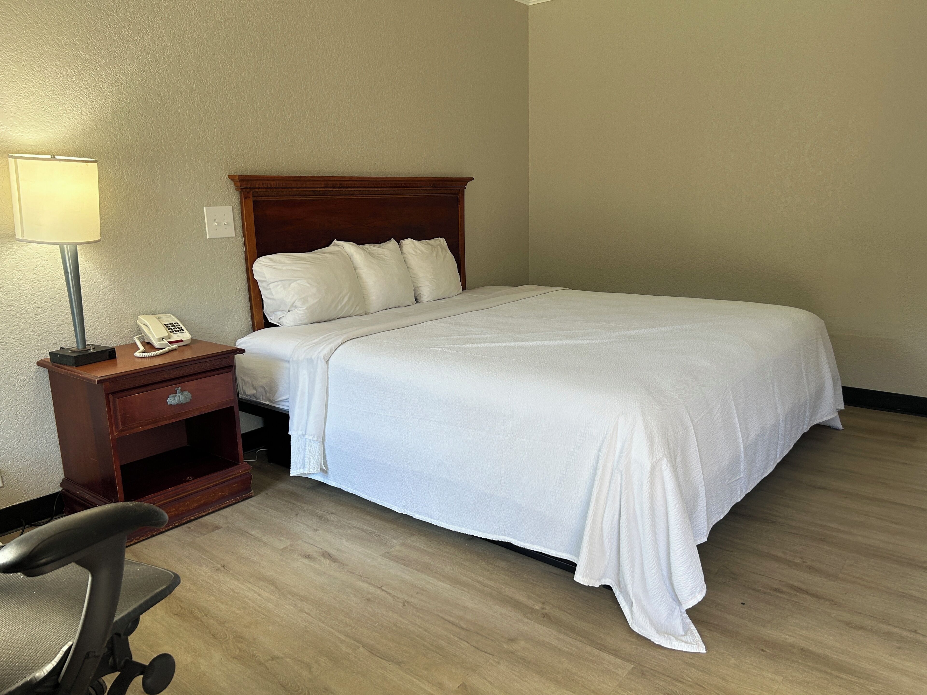 A hotel room with a bed, a nightstand with a lamp, and a chair.