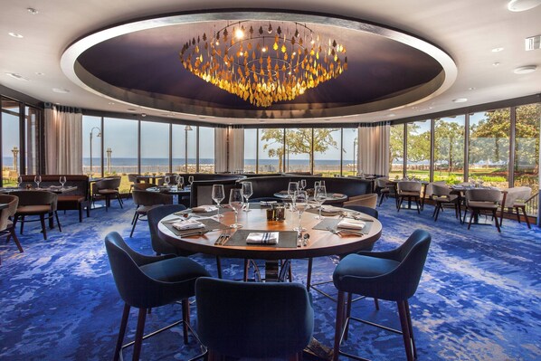 A round table with chairs and a chandelier in a room with large windows and a view of the sea. - Grand Hotel Golf Resort & Spa, Autograph Collection (Fairhope)