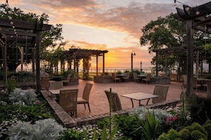 An outdoor patio area with wicker furniture and a view of the sunset over the water. - Grand Hotel Golf Resort & Spa, Autograph Collection (Fairhope)