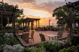 Un patio al aire libre con mobiliario de mimbre y vistas al atardecer sobre el agua.
