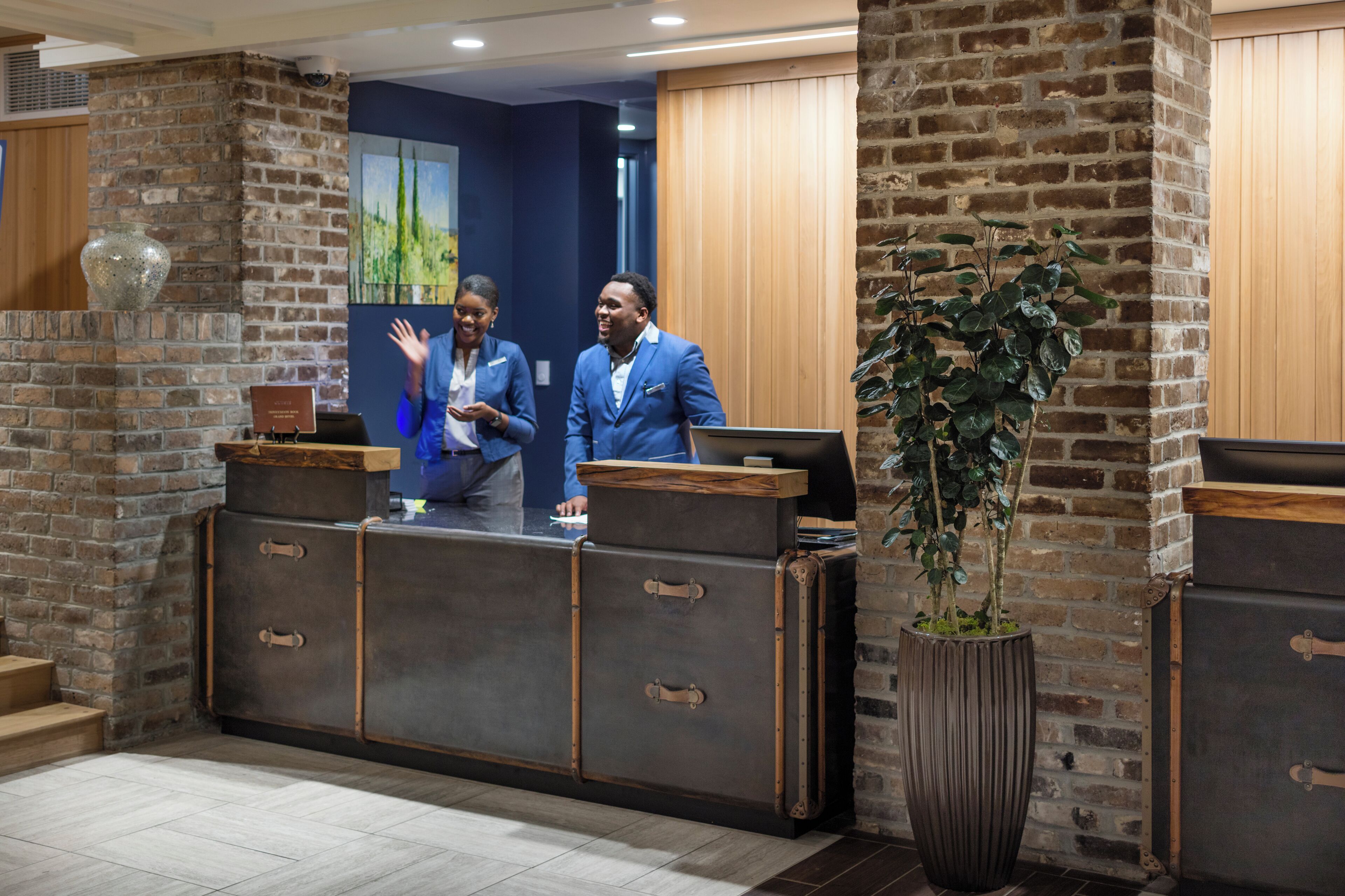 A reception desk with a rustic brick wall, a large potted plant, and a wooden counter.