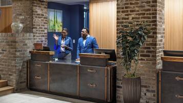 A reception desk with a rustic brick wall, a large potted plant, and a wooden counter.