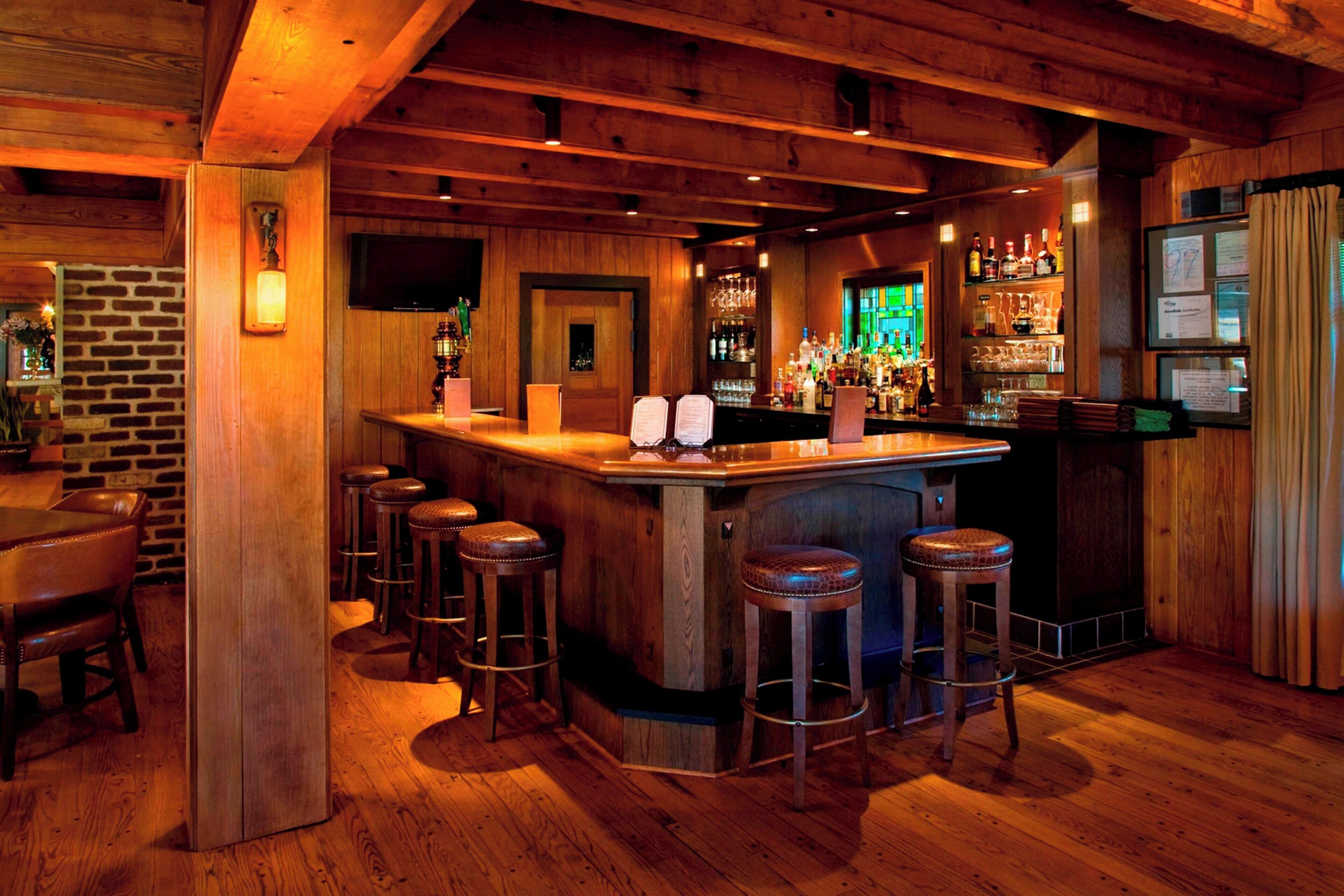 A bar area with wooden beams, a brick wall, and a bar counter with stools.