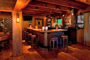 A bar area with wooden beams, a brick wall, and a bar counter with stools.