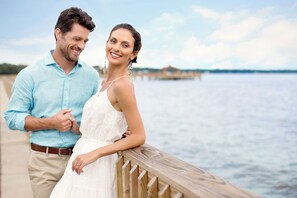 A couple standing on a wooden pier with a body of water and a distant shoreline in the background. - Grand Hotel Golf Resort & Spa, Autograph Collection (Fairhope)
