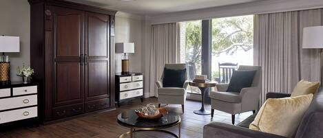 A modern living room with a dark wood cabinet, a round coffee table, a sofa, and a view of the outdoors through large windows.