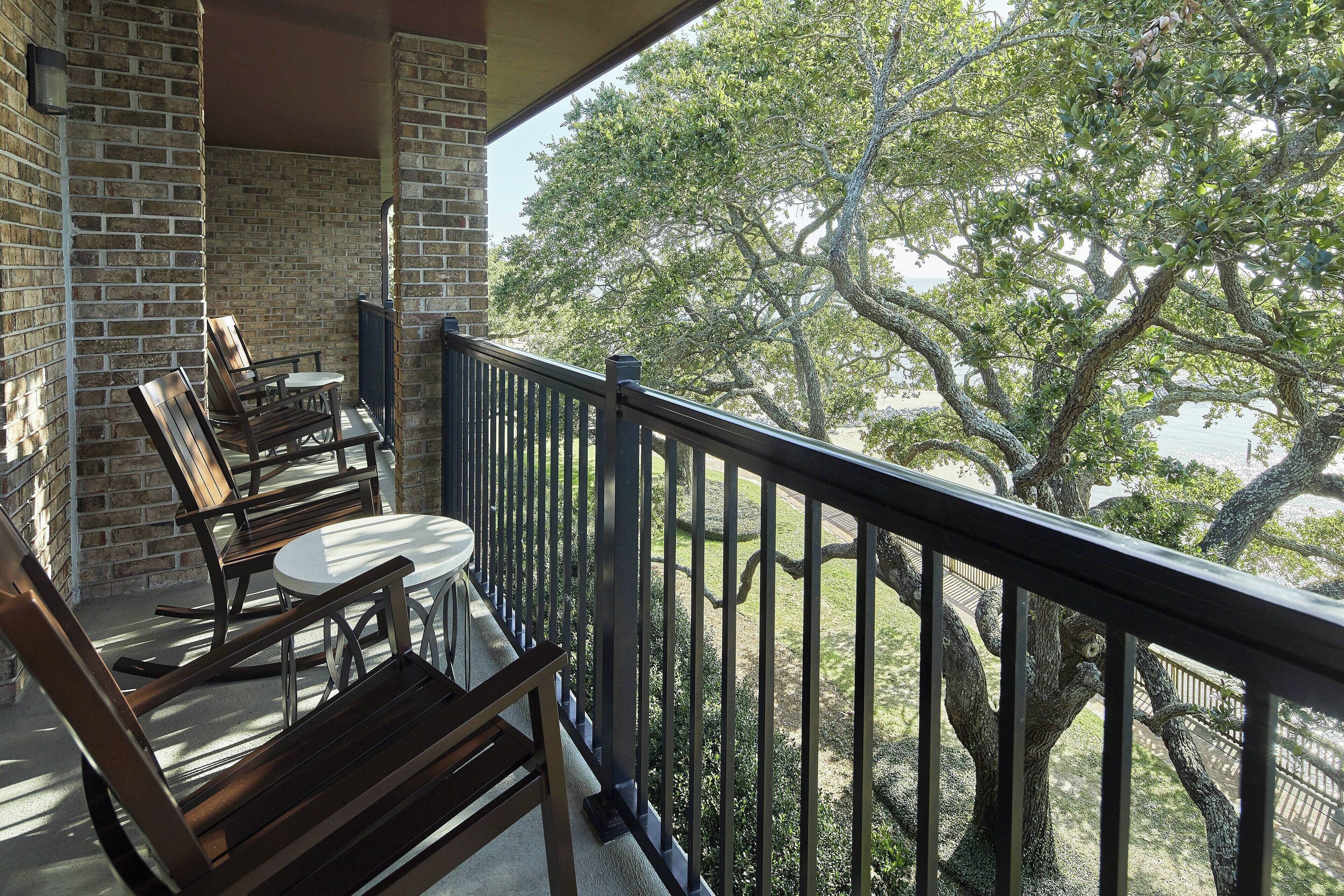 A balcony with brick walls, wooden furniture, and a view of trees.