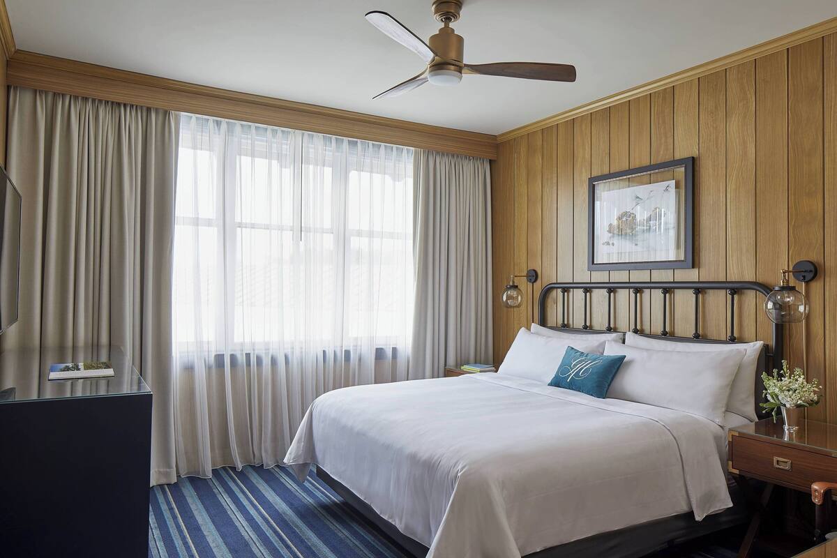 Une chambre d’hôtel équipée d’un lit, d’un bureau, d’un ventilateur de plafond et d’une fenêtre avec des rideaux.