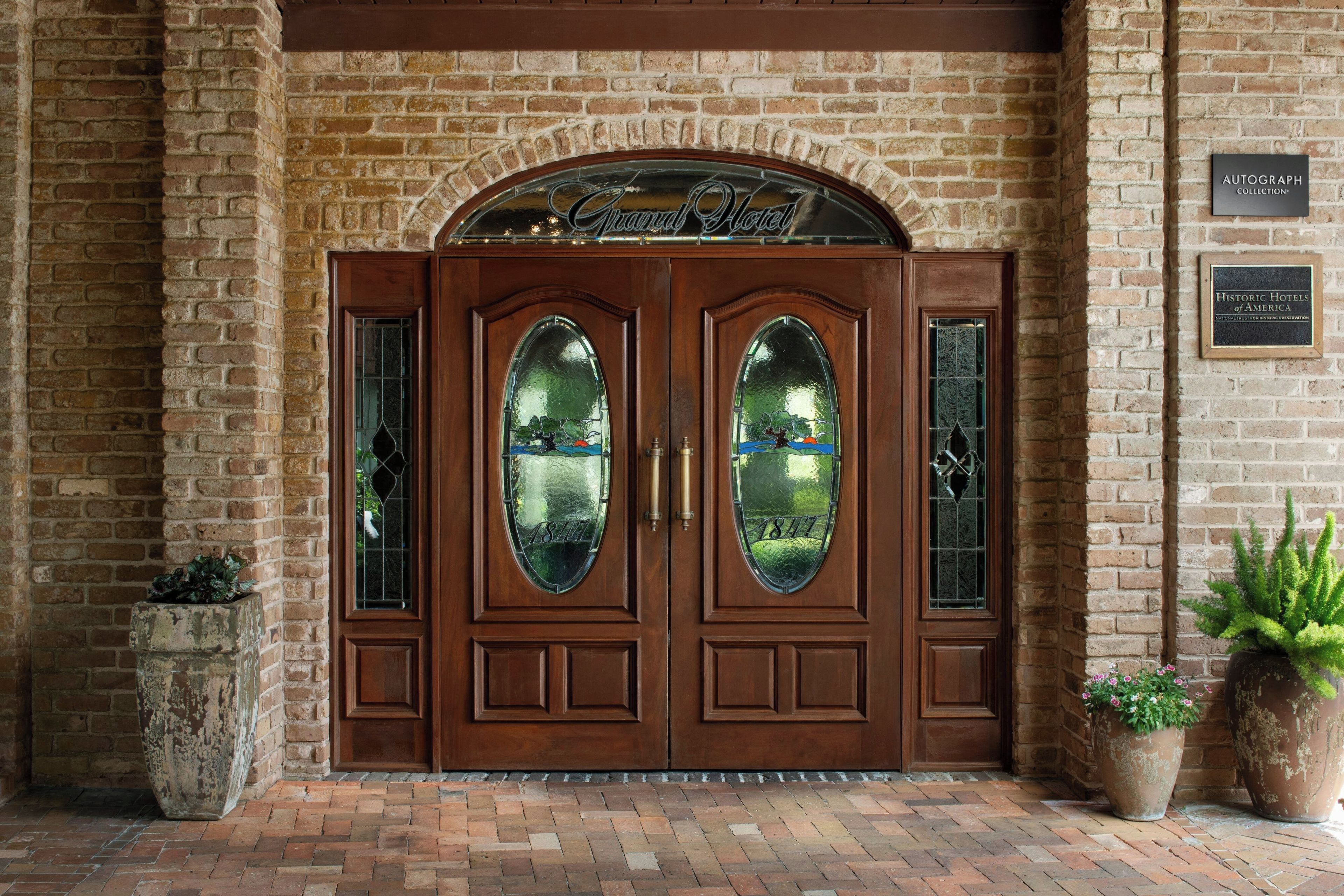 A brick building with a double wooden door featuring glass panels and a sign above stating 'Autograph Collection'.