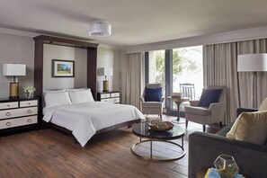 A hotel room with a large bed, two armchairs, a small table, and a view of the outdoors. - Grand Hotel Golf Resort & Spa, Autograph Collection (Fairhope)