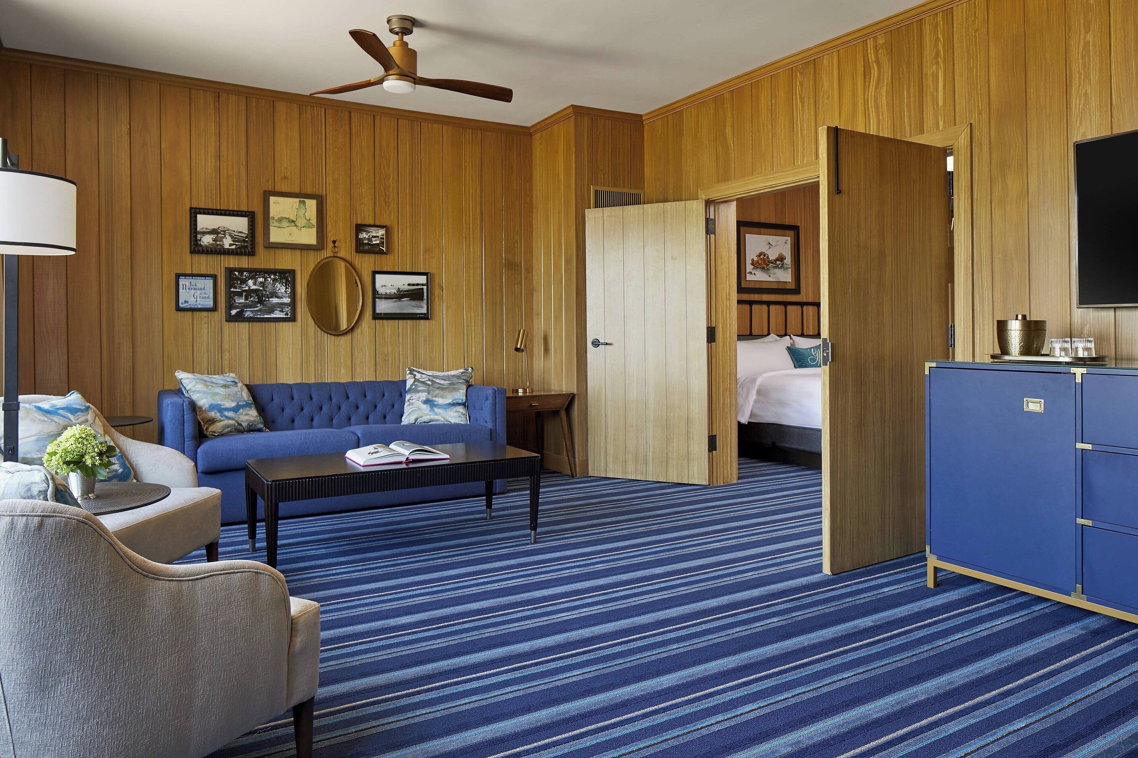Una habitación de hotel con alfombra azul a rayas, sofá azul, armario de madera y cama con cabecero azul.