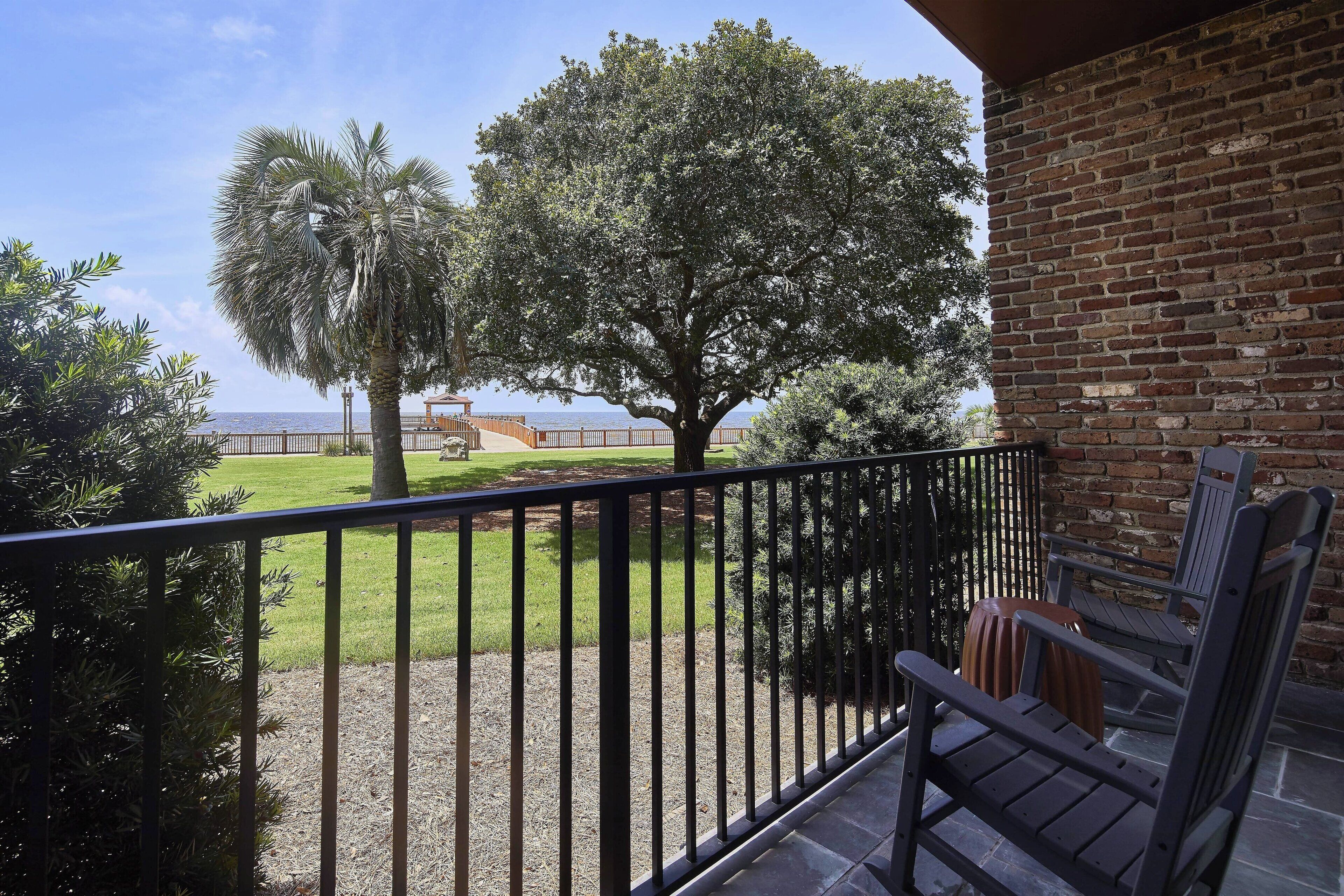 A balcony with a view of a grassy area and trees, a brick wall, and a wooden chair.