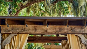 A covered outdoor seating area with a wicker sofa, beige curtains, and a view of the beach. - Grand Hotel Golf Resort & Spa, Autograph Collection (Fairhope)
