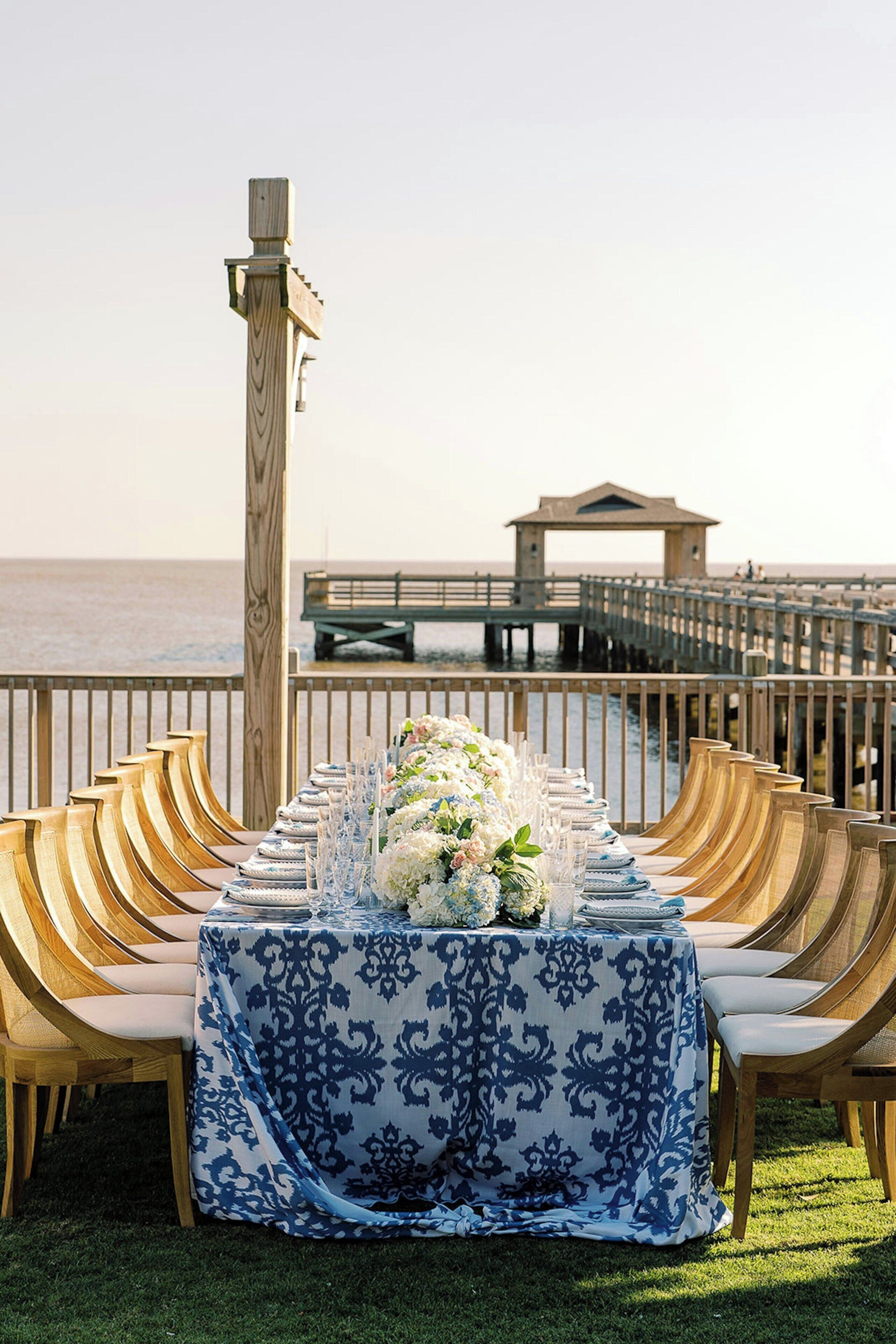 Mesa lista para una comida con sillas en una terraza con vista al océano.